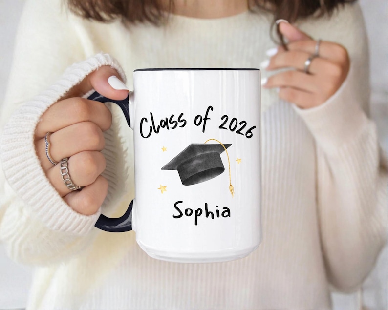 White and black ceramic mug with a black graduation cap and the text "Class of 2026" and "custom name" in black.