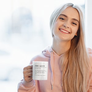 May include: A white ceramic mug with a black inscription that reads "Boss Lady" with a heart symbol. The mug is held by a person wearing a pink hoodie.