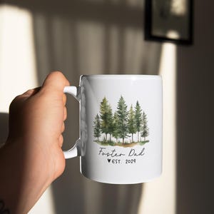 Puede incluir: Taza de cer&aacute;mica blanca con una ilustraci&oacute;n de acuarela de un bosque y el texto "Foster Dad &hearts; EST. 2024"