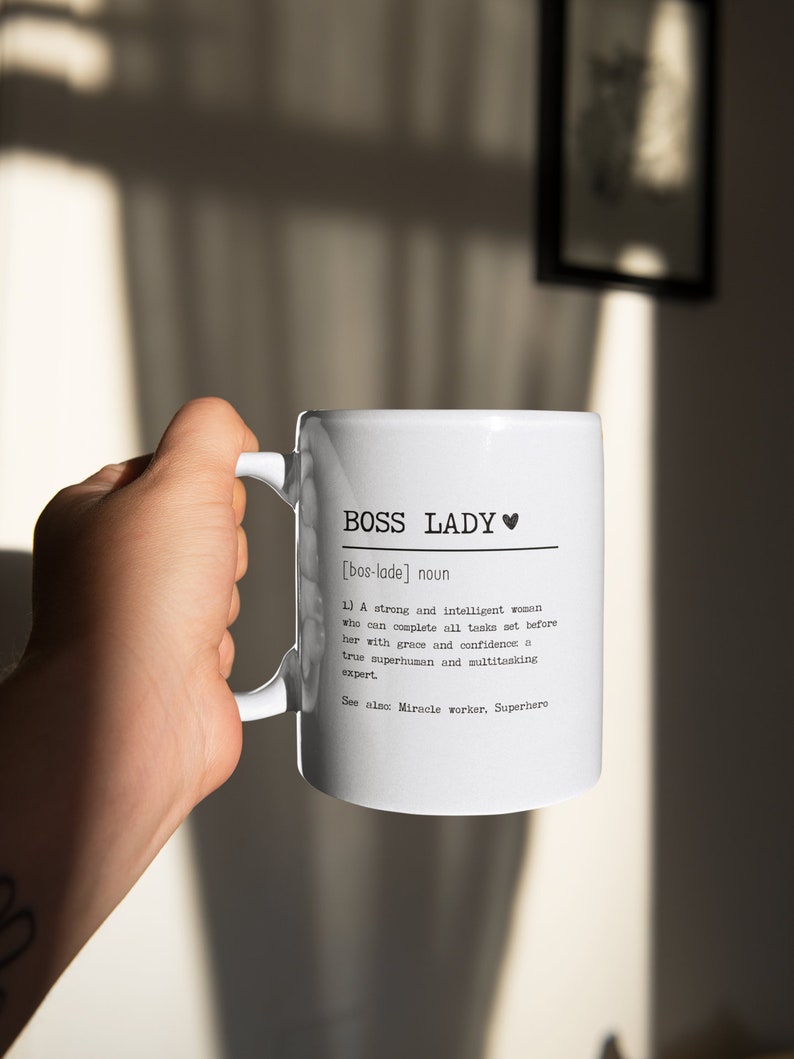 May include: White ceramic mug with a black design that reads "BOSS LADY [bos-lade] noun 1) A strong and intelligent woman who can complete all tasks set before her with grace and confidence a true superhuman and multitasking expert See also: Miracle worker, Superhero"