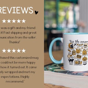 May include: White ceramic mug with a light blue handle and interior. The mug features the phrase "'tis the season" and Halloween-themed illustrations, including a witch, skull, and pumpkin. The mug is sitting on a book.
