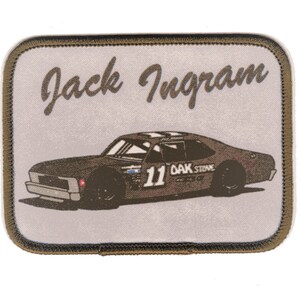 Peut inclure: Écusson rectangulaire avec une voiture de course marron, le numéro 11 et le texte "OAK STAVE". Le nom "Jack Ingram" est écrit au-dessus de la voiture en cursive. L'écusson a un fond beige clair et une bordure marron.