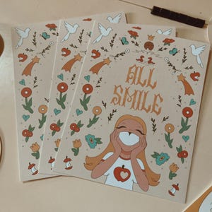 May include: Four beige art prints with a floral and celestial design. Each print features the text "ALL SMILE" and an illustration of a smiling girl. The prints are decorated with doves, shooting stars, and flowers.