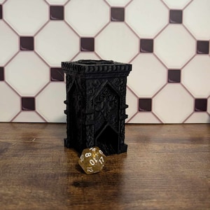 May include: Black 3D printed dice tower with intricate details and a gold glitter dice with white numbers 1 through 12.