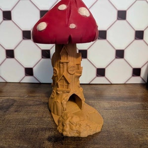 May include: A 3D printed mushroom house with a red and white mushroom cap and a brown tree trunk with windows and a door. The house is sitting on a brown base.