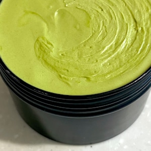 organic green matcha green tea whipped Shea butter in a black container. The creamy butter has a smooth, silky texture and is swirled in a circular pattern. natural skincare natural haircare