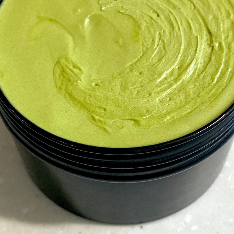 organic green matcha green tea whipped Shea butter in a black container. The creamy butter has a smooth, silky texture and is swirled in a circular pattern. natural skincare natural haircare