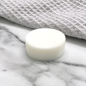 May include: A white round bar of soap on a marble surface.