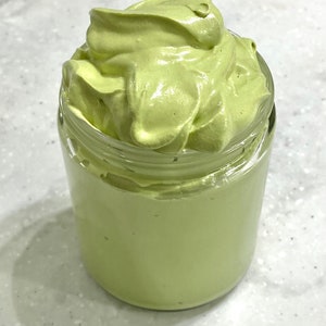 May include: A glass jar filled with a light green whipped cream-like substance.