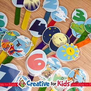 May include: A collection of educational flashcards for kids, featuring numbers, illustrations of nature elements, and animals. The cards are on colorful sticks, with images of the sun, moon, birds, and sea creatures. The "Creative for Kids" logo is visible.