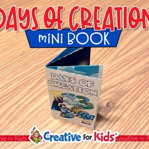 May include: A small, open mini-book titled "DAYS OF CREATION" in red lettering. The book's cover displays the same title and colourful illustrations. The words "MINI BOOK" are in blue. The book is on a wooden surface.