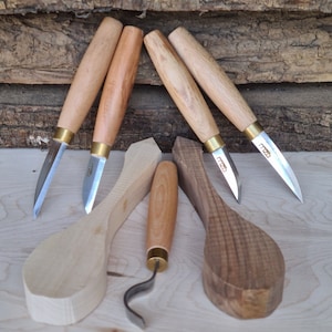 May include: Five wood carving tools with wooden handles and metal blades. The tools are arranged on a light wood surface with two wooden bowls.