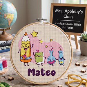 Puede incluir: Un bastidor de bordado redondo de madera con un diseño de punto de cruz de un lápiz amarillo, un libro verde y dos matraces de laboratorio azules con caras. El nombre Mateo está bordado en morado debajo de los personajes.