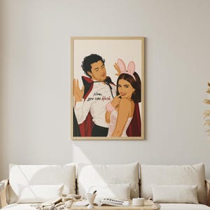 Stylized digital wall art featuring a romantic college couple inspired by a popular sports romance book series. The artwork shows a dark-haired male character dressed in a playful vampire costume beside a smiling female character wearing pink bunny ears. The illustration includes the quote "Now, you can blush" and is rendered in a modern minimalist portrait style with clean lines and soft colors. Perfect for romance readers, book lovers, and contemporary literary-inspired home decor.