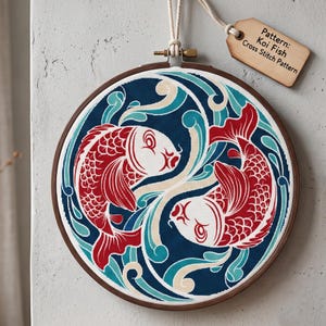 May include: A circular wooden embroidery hoop containing a cross stitch pattern of two red koi fish swimming in a circular motion against a dark blue background with teal and cream water swirls. A wooden tag attached by string reads: Pattern: Koi Fish Cross Stitch Pattern.