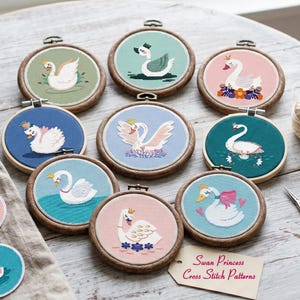 May include: A collection of nine cross-stitch patterns featuring swan designs in wooden embroidery hoops. Each hoop has a different background color, including blue, pink, and green, with a swan wearing a crown. The tag reads "Swan Princess Cross Stitch Patterns."