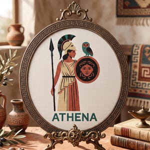 May include: A circular needlepoint display featuring a depiction of Athena in a helmet, holding a spear and a shield with a Medusa emblem, accompanied by an owl. The word ATHENA is printed below in dark green. The piece is set in an ornate bronze frame.