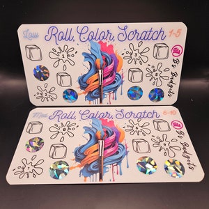 May include: Two colorful game cards with the text "Roll, Color, Scratch" and "B & S Budgets". The cards are divided into sections with paint splatters and paintbrushes. Each section has a number and a blank square.