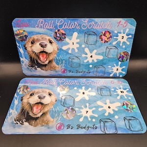 May include: Two blue and white cards with a cartoon otter on each. The cards are for a game called "Roll, Color, Scratch". The first card has the numbers 1-5 and the second card has the numbers 6-10. Each card has a holographic sticker on it.