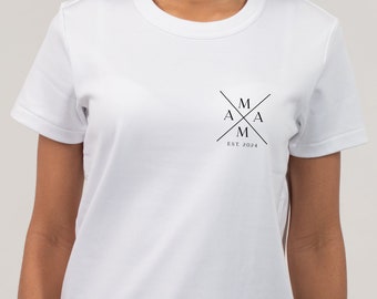 Op de afbeelding: Wit T-shirt met een zwart logo met de tekst "M A M A M" en "EST. 2024"