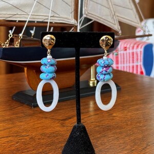May include: A pair of dangle earrings with a white oval shaped charm and turquoise and purple patterned beads.