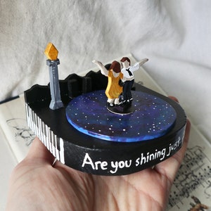 May include: A hand-painted wooden music box featuring a couple dancing on a stage with a starry night backdrop. The music box plays the song "Are you shining just for me?" from the musical "Dirty Dancing".