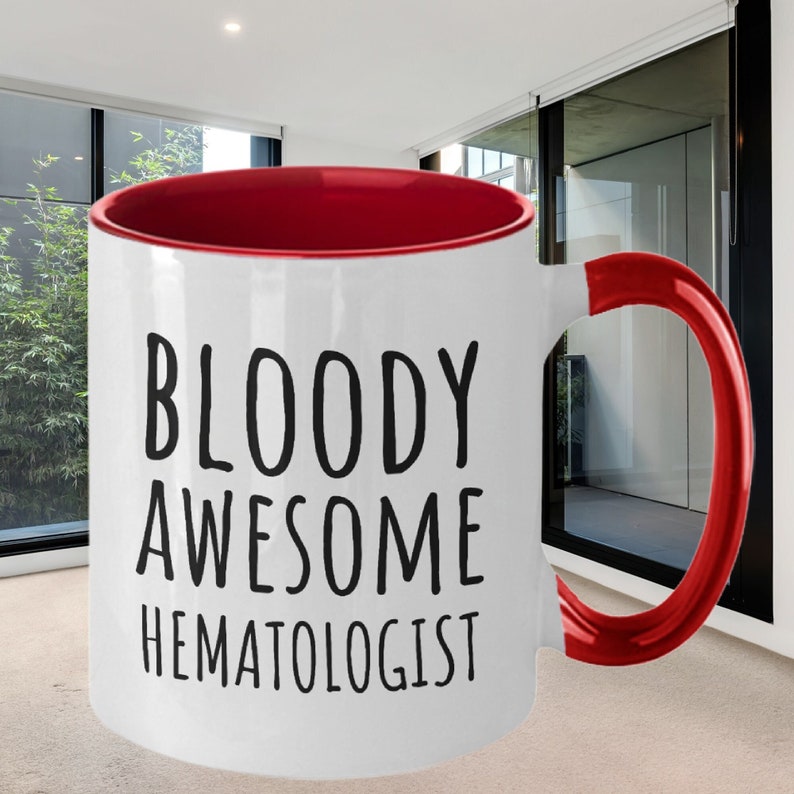 May include: White ceramic coffee mug with a red rim and handle. The mug has black text that reads "BLOODY AWESOME HEMATOLOGIST".