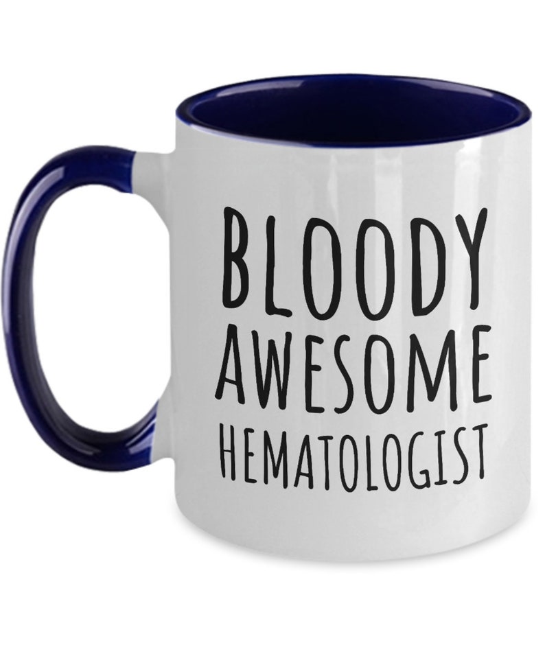 May include: White ceramic coffee mug with a blue rim and handle. The mug has black text that reads "BLOODY AWESOME HEMATOLOGIST".