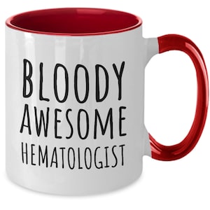May include: White coffee mug with a red rim and handle. The mug has black text that reads "BLOODY AWESOME HEMATOLOGIST".