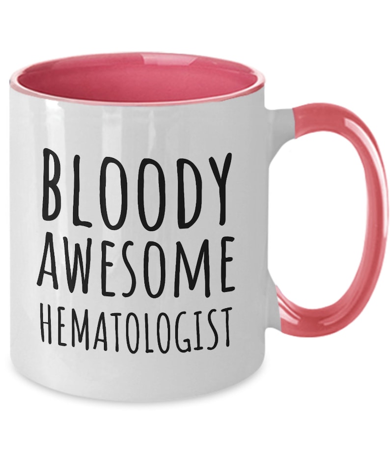 May include: White coffee mug with a pink rim and handle. The mug has black text that reads "BLOODY AWESOME HEMATOLOGIST".