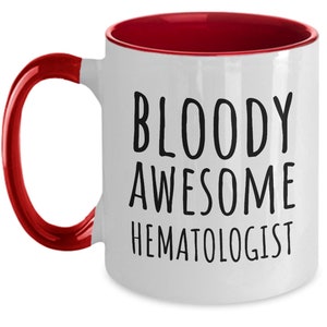 May include: White coffee mug with a red rim and handle. The mug has black text that reads "BLOODY AWESOME HEMATOLOGIST".