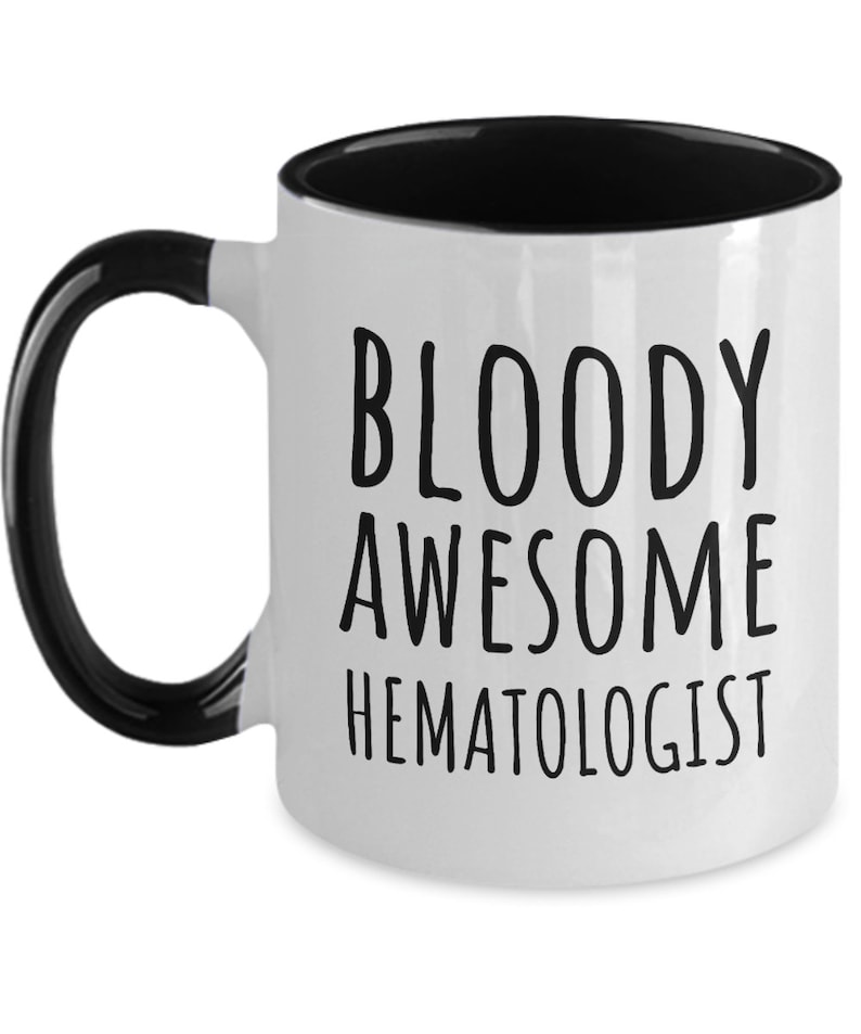 May include: White coffee mug with a black handle and black rim. The mug has black text that reads "BLOODY AWESOME HEMATOLOGIST".