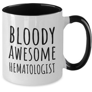 May include: White coffee mug with a black rim and handle. The mug has black text that reads "BLOODY AWESOME HEMATOLOGIST".