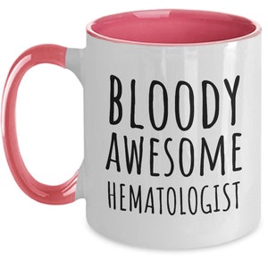 May include: White coffee mug with a pink rim and handle. The mug has black text that reads "BLOODY AWESOME HEMATOLOGIST".