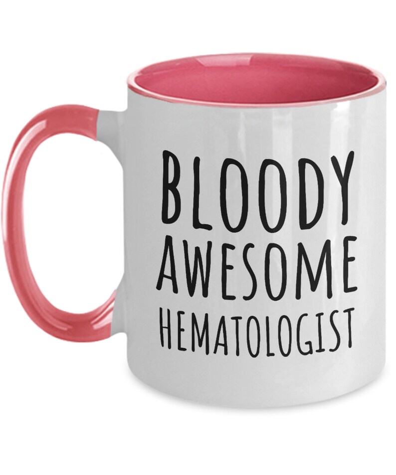 May include: White coffee mug with a pink rim and handle. The mug has black text that reads "BLOODY AWESOME HEMATOLOGIST".