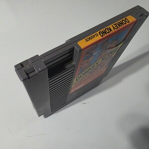 Puede incluir: Un cartucho de videojuego gris de Donkey Kong Classics. La etiqueta presenta a Donkey Kong y Mario en una ilustraci&oacute;n colorida. El cartucho est&aacute; en &aacute;ngulo, mostrando el lado con el t&iacute;tulo del juego y la etiqueta "Classics".