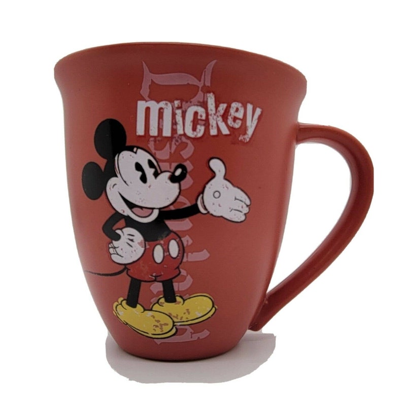 May include: Red ceramic coffee mug with a cartoon image of Mickey Mouse in a red and black outfit. The mug has the word "mickey" printed on it in white.