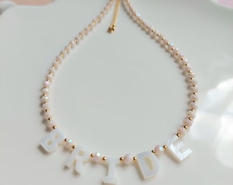 May include: A white beaded necklace with a gold chain and a white "BRIDE" charm.
