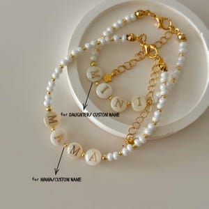 May include: Two beaded bracelets featuring white pearls and gold-tone accents. One bracelet displays the word MAMA in gold letters, and the other displays the word MINI in gold letters. Both include gold-tone lobster clasps and extender chains.
