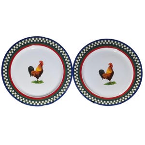 Puede incluir: Dos platos de cerámica blanca con diseño de gallo. Cada plato presenta una ilustración de gallo en el centro, rodeada por una banda roja y verde, y un borde a cuadros azul y blanco. Adecuados para la decoración de cocina o comedor.