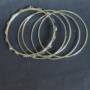 May include: A set of five thin, circular metal bangles. Three of the bangles feature a smooth, polished finish with small, evenly spaced decorative metal beads along the outer edge, while two bangles have a textured, twisted metal surface.
