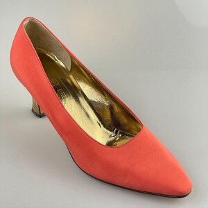 May include: A pair of coral-colored satin pumps with a pointed toe and a low, wooden heel.