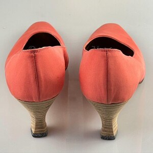 May include: A pair of coral colored high heeled shoes with a low heel. The shoes are made of a soft fabric and have a pointed toe.