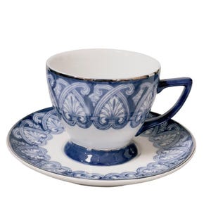 May include: A white teacup and saucer set with a blue decorative pattern. The teacup has a silver rim and a blue handle. The saucer has a matching design. The set is designed for serving tea.