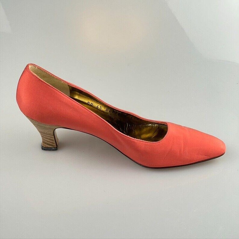 May include: A pair of coral pink satin pumps with a low heel and a pointed toe.