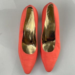 May include: A pair of coral-colored satin pumps with a pointed toe and a low heel. The shoes are made by Bruno Magli and are made in Italy.