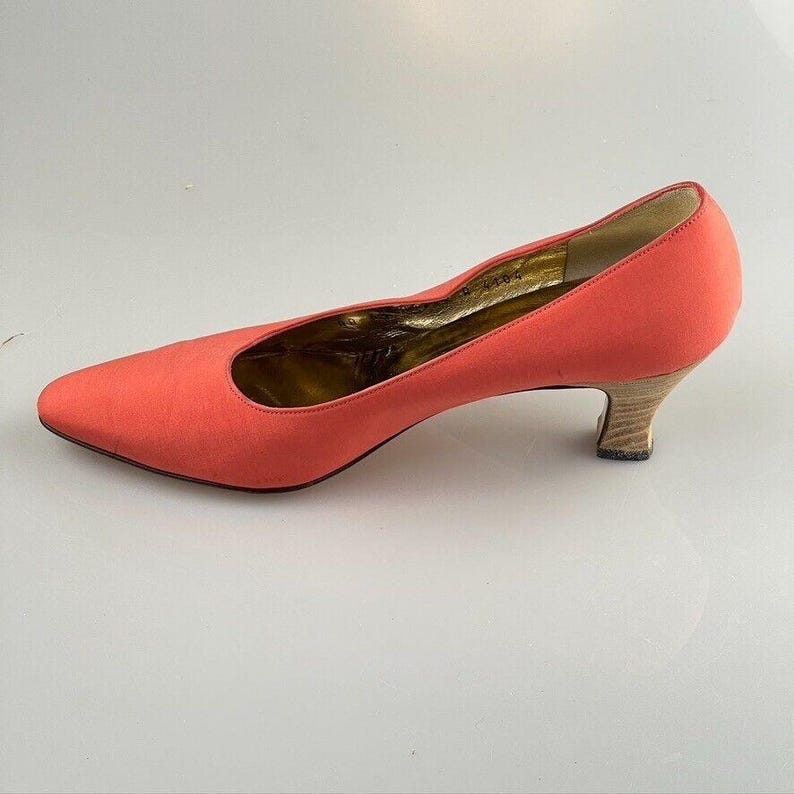 May include: A pair of coral pink satin pumps with a low, wooden heel.