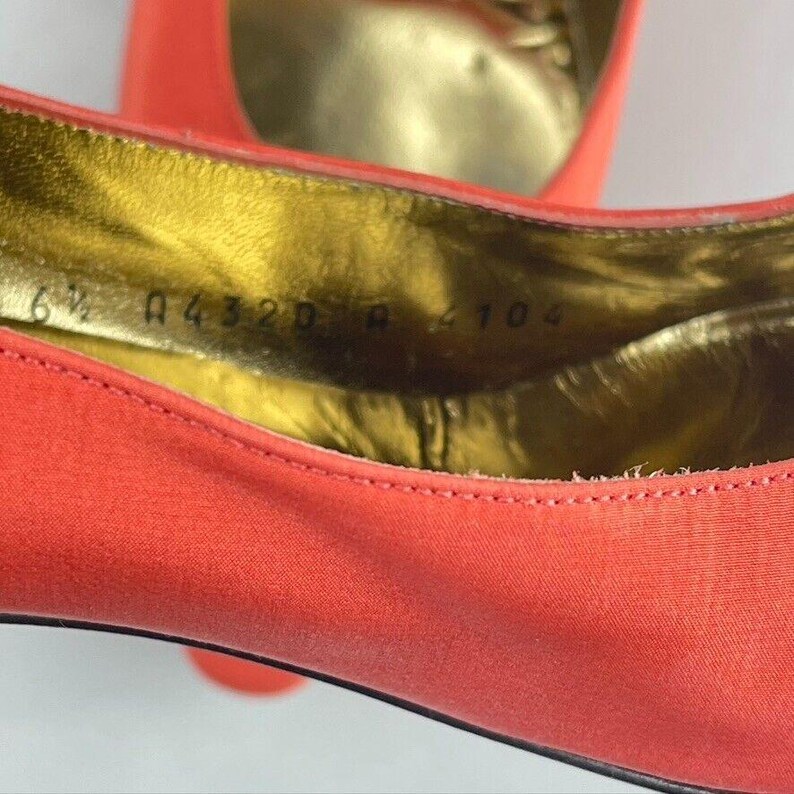 May include: Close-up of the inside of a red satin shoe with a gold insole. The size 6 1/2 is printed on the insole along with other numbers.