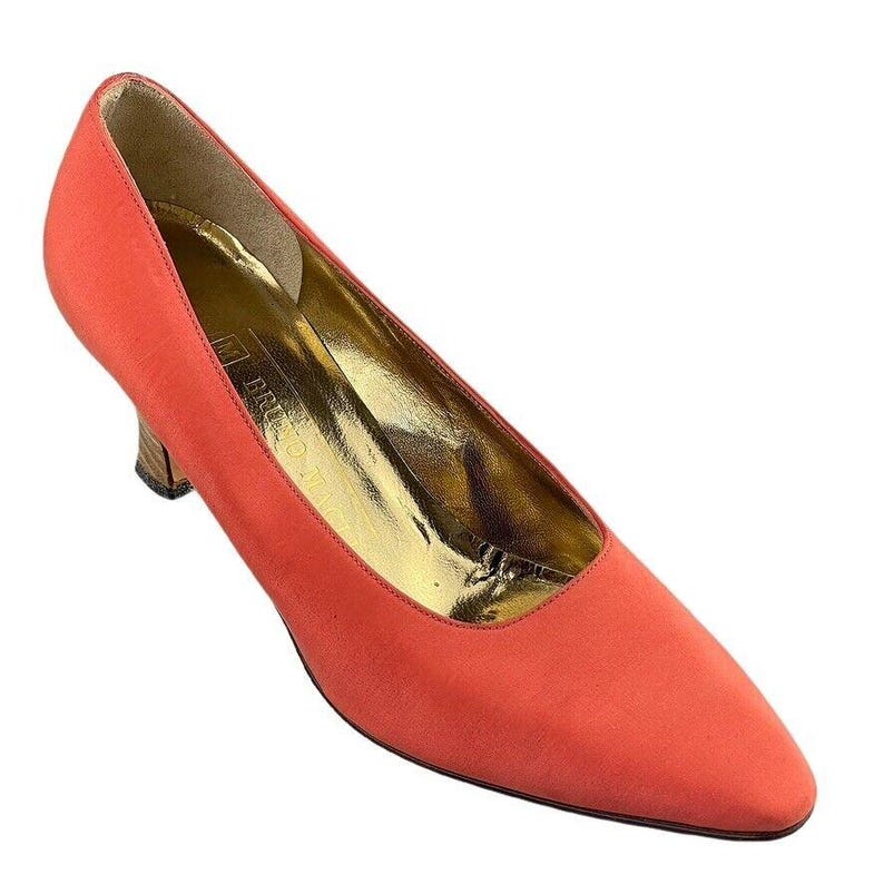 May include: A pair of coral-colored suede pumps with a low heel. The shoes have a pointed toe and a gold leather lining.