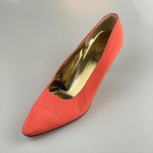 May include: A pair of coral-colored pointed-toe pumps with a gold lining. The shoes are made of a soft, smooth fabric.